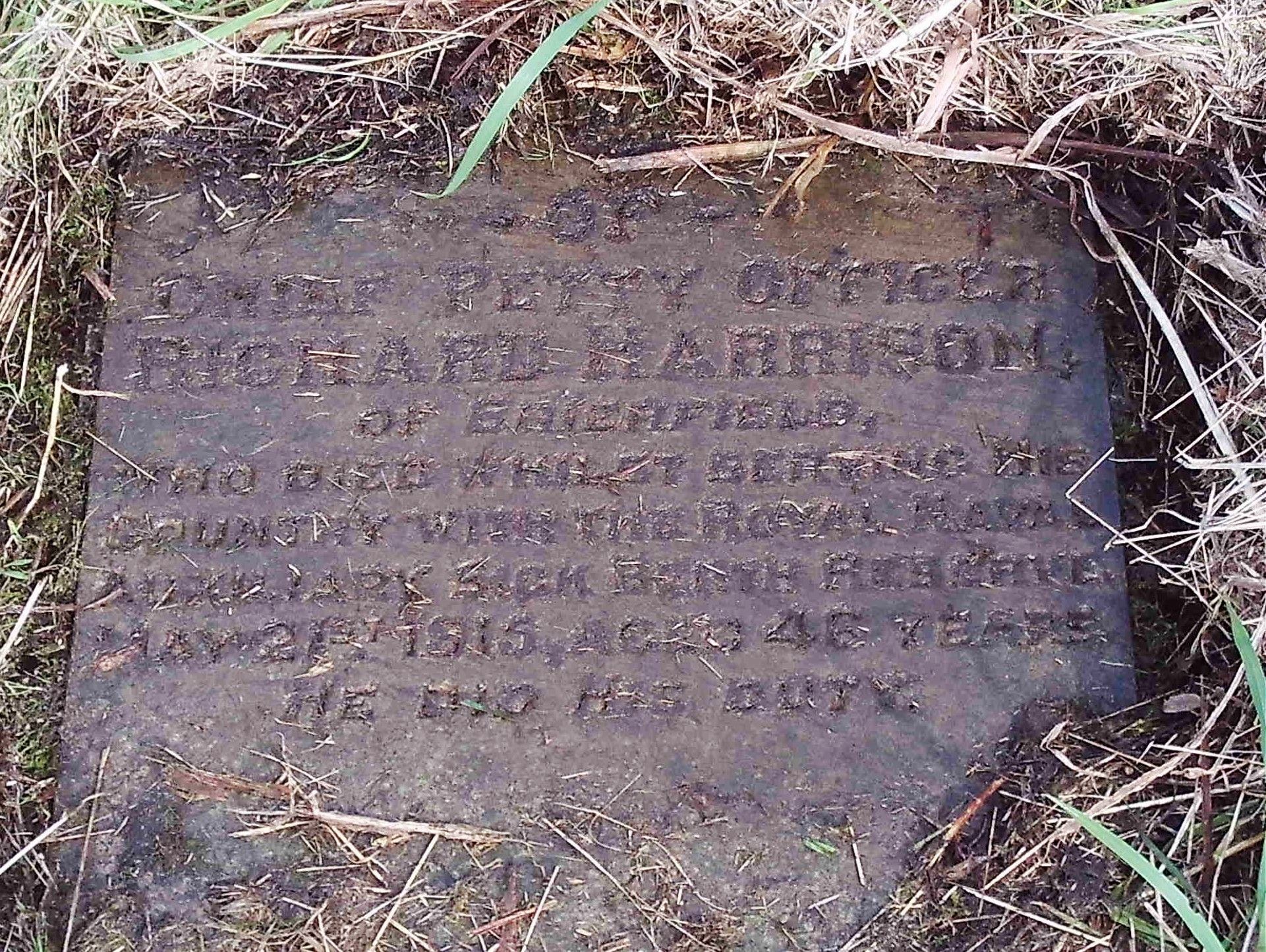 A stone flag with an inscription on it, after being cleared of soil and grass.
