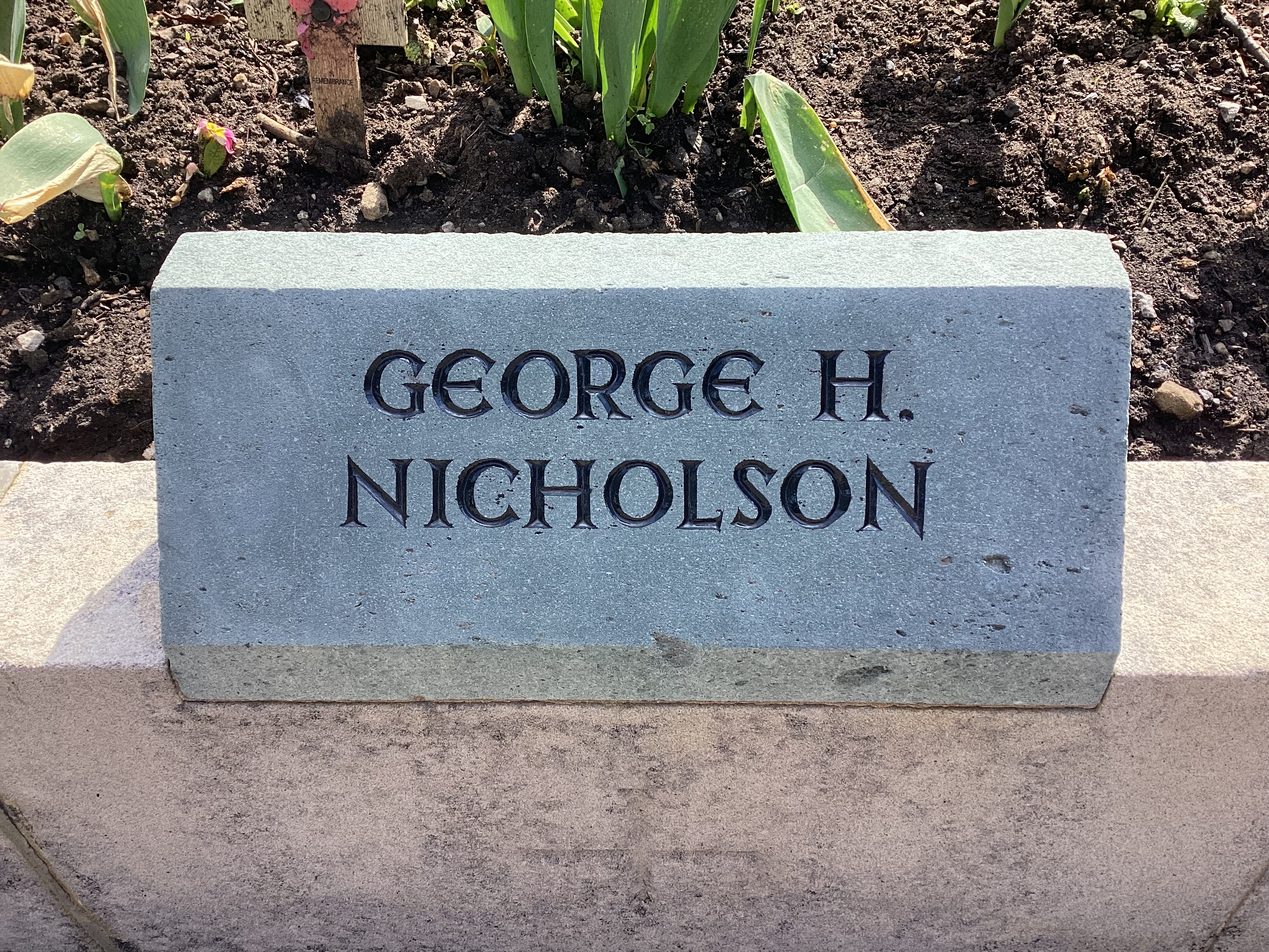 A green slate memorial stone with the name GEORGE H. NICHOLSON engraved in black lettering.