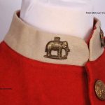 A White collar on a red frock with a close up of the elephant and howdah badge of the West Riding Regiment.