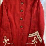 A bright scarlet uniform jacket of the Leicestershire Regiment. It is all red apart from a white collar and has four brass buttons and white lacing on each cuff. On the collar are two badges with the Leicester Tiger badge. On the left sleeve are two good conduct badges which are an inverted chevron with the point upwards.