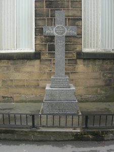 A light grey coloured granite memorial cross with a stepped base. On the base stones are the names of five men, two who died in the first World War and three men who died in the Second World War.