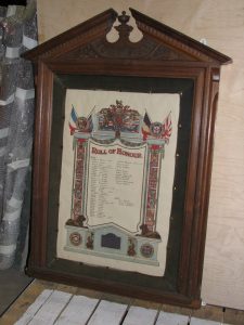 A wooden framed and glazed roll of honour. On the paper is a list of 45 names of the Exley Head church parishioners who served, including the names of those who died in both wars. There are flags and scrolls at the top with coloured pillars at the sides and lion emblems at the bottom.