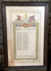 An Oak framed and glazed Roll of Honour. The inscription is bordered by a geometric pattern on green background and topped by the flags of the Home Nations. Above are the Union Flag and Naval ensign. On the paper is a list of names of the St. John's church parishioners who served, plus the names of those who died in the First World war.