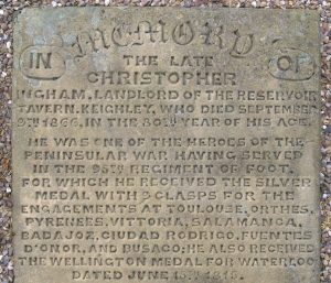 A sandstone grave slab set in gravel, bearing the following inscription: In memory of the late Christopher Ingham, Landlord of the Reservoir Tavern, Keighley, who died September 9th 1866, in the 80th Year of his age.He was one of the heroes of the Peninsular War having served in the 95th Regiment of Foot, for which he received the Silver Medal with 9 clasps for the engagements at TOULOUSE, ORTHES, PYRENEES, VITTORIA, SALAMANCA, BADAJOS, CUIDAD RODRIGO, FUENTES D'ONOR AND BUSACO: he also received the Wellington Medal for Waterloo. Dated June 12th 1815.