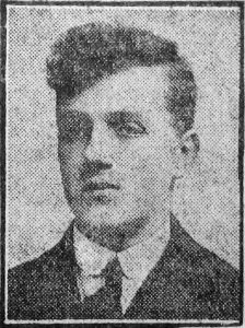 A newspaper photo of a man's head and shoulders. He is wearing a dark jacket with a shirt and tie.