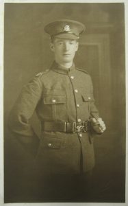A studio photograph of a soldier in uniform, wearing a service cap with the badge of the Duke of Wellington's West Riding Regiment. He is standing and holding a walking cane under his arm.