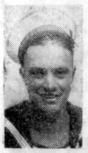 Portrait photo of a man's head and shoulders. This is of poor quality from a newspaper in 1914 and he is wearing Royal Navy Uniform with his white sailor's cap pushed far back from his forehead. He is facing the camera and smiling.