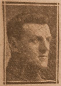 A newspaper photo from 1918 of a man wearing army uniform. Head and shoulders only. He is clean shaven with short hair and is not wearing a cap.