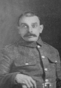 A studio photograph of a soldier in uniform sitting in a chair. From a family group photograph.