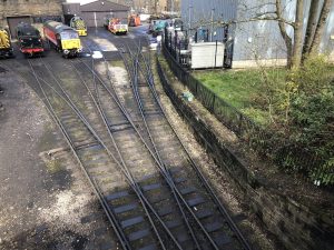 A scene in a railway yard from a bridge above. It shows several railway lines and a curved wall on the right. There are a number of engines on the left.