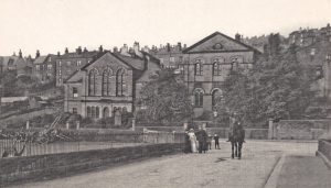 Station Road at Haworth. On the left is a fenced area used for offloading railway trucks. There are a number of horse carts stored against the wall. In the distance is the Methodist church and Sunday School.