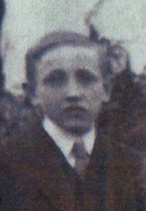 A slightly out of focus image of a young man dressed in a suit, shirt and tie. He is clean shaven and facing the camera.