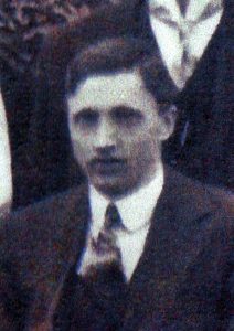 A slightly out of focus image of a young man dressed in a suit, shirt and tie. He is clean shaven and facing the camera.