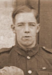 A portrait photograph of a British Army soldier in uniform. He is wearing an army jacket from the Great War period and has a military medal ribbon sewn above his left breast pocket.