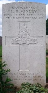A white headstone with details of Gunner Lewis Ainley. The inscription reads: 785975 L. E. Ainley Royal Field Artillery 6th March 1917 Age 20 He Finally Passed Out Of The Sight Of Men By The Path Of Duty.