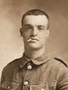 A photograph of a soldier in uniform. He is not wearing a cap but has a cigarette in his mouth.