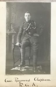 A studio photograph of a man sitting on the edge of a table. He is wearing British Army uniform of the Great war period.