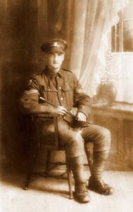 A studio portrait of a British Army soldier in full uniform and cap. He is wearing the Military medal ribbon and is seated in a chair.