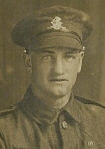 A portrait photo of a British Army soldier in a studio. He is in the West Riding Regiment and is wearing a cap with the regimental badge on it and facing the camera.