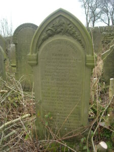 An arched topped stone gravestone with a large panel of the Greenwood family's names.