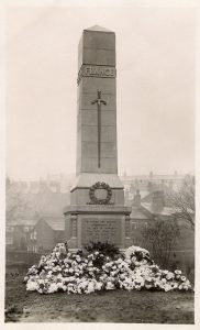 A black and white photograph of a large grey stone obelisk with a stepped base and the names of 100 men in lettering on three sides.